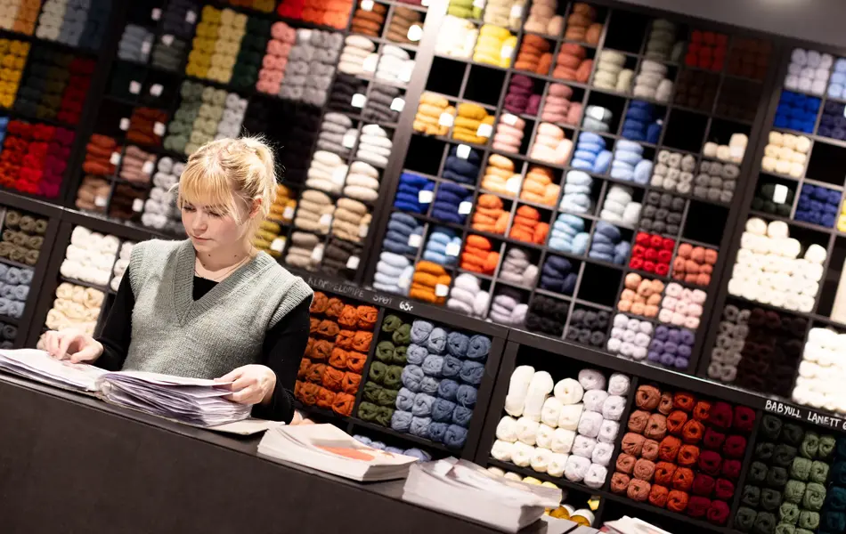 Dame i butikk som ser på strikkeoppskrifter