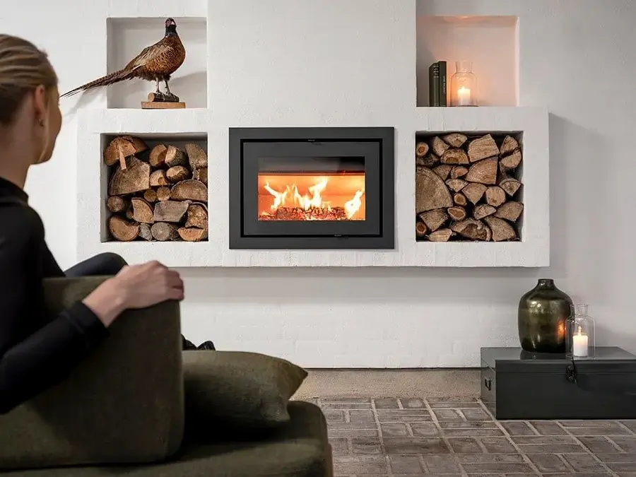 Dame med svart genser sitter på en grønn sofa og varmer seg foran peisen