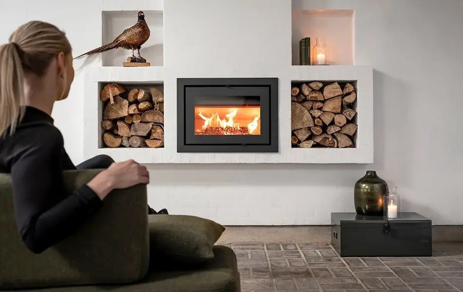 Dame med svart genser sitter på en grønn sofa og varmer seg foran peisen