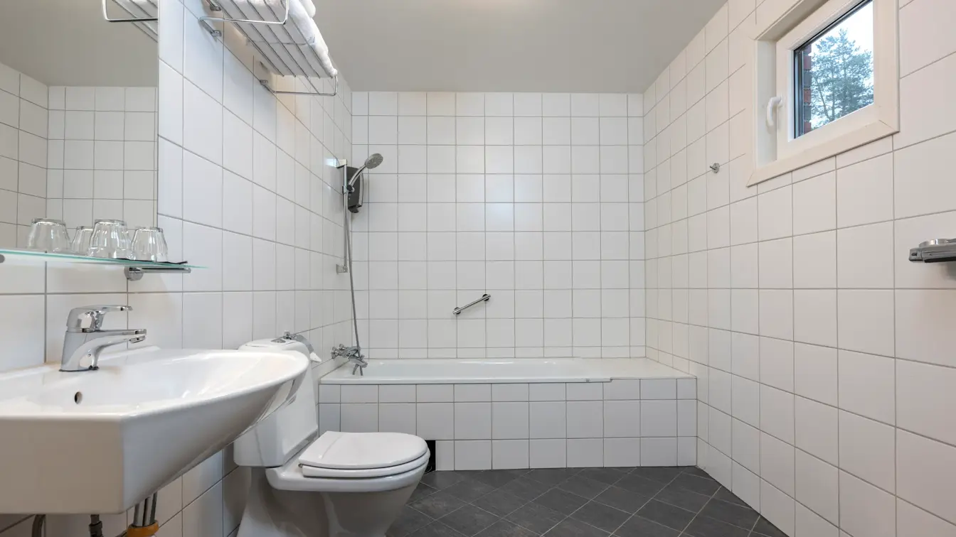 Bad med badekar, toalett, servant med speil og hvite fliser.