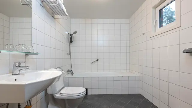 Bad med badekar, toalett, servant med speil og hvite fliser.