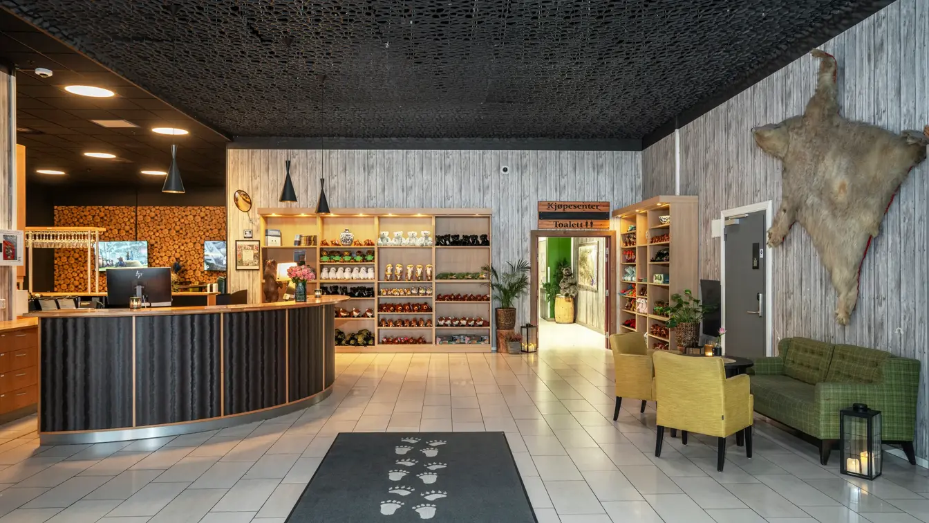 Lobbyområde med resepsjonsdisk, butikkhyller med varer, grønn sofa og gule stoler