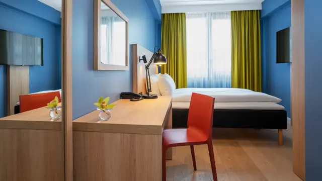 Speil. skrivebord med rød stol, blå vegger, dobbeltseng og gule gardiner i dobbeltrom på Thon Hotel Astoria