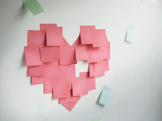 Blank pink sticky notes sticked in a heart shape on wall.
