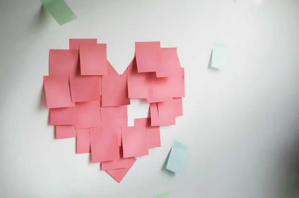 Blank pink sticky notes sticked in a heart shape on wall.