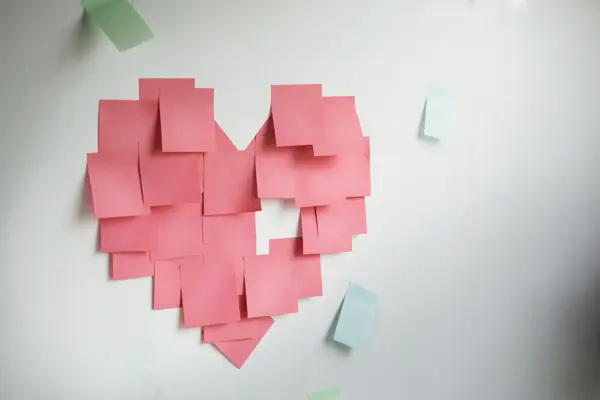 Blank pink sticky notes sticked in a heart shape on wall.