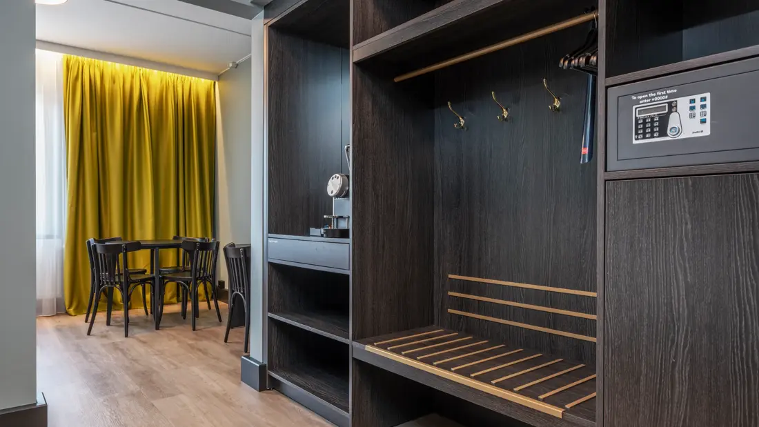 Business rom med åpen garderobe, safe, Nespresso maskin, spisebord med stoler og gule gardiner.