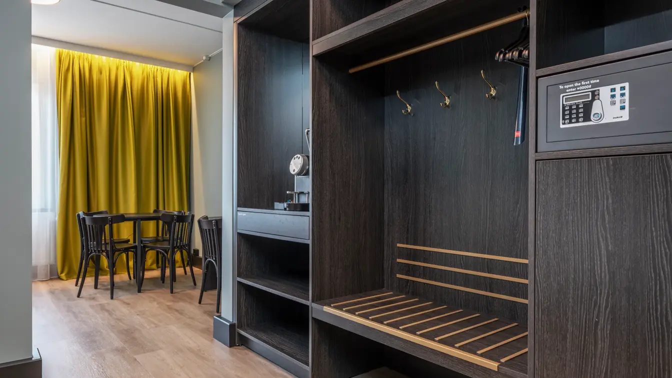 Business rom med åpen garderobe, safe, Nespresso maskin, spisebord med stoler og gule gardiner.
