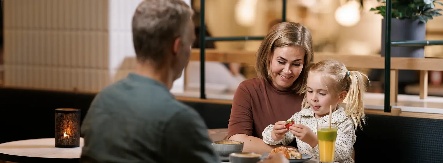 En mann, en kvinne og et barn sitter ved et bord på en kafé, barnet sitter på fanget til kvinnen 