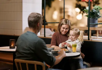 En mann, en kvinne og et barn sitter ved et bord på en kafé, barnet sitter på fanget til kvinnen 
