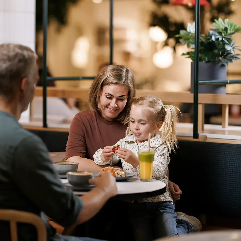 En mann, en kvinne og et barn sitter ved et bord på en kafé, barnet sitter på fanget til kvinnen 