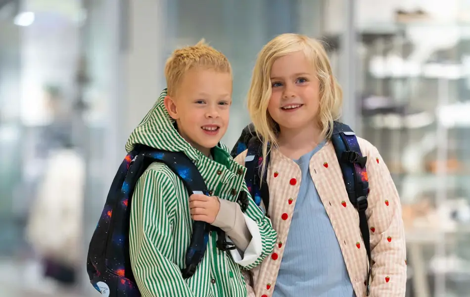 Gutt og jente står ved siden av hverandre på et kjøpesenter med yttertøy og skolesekker