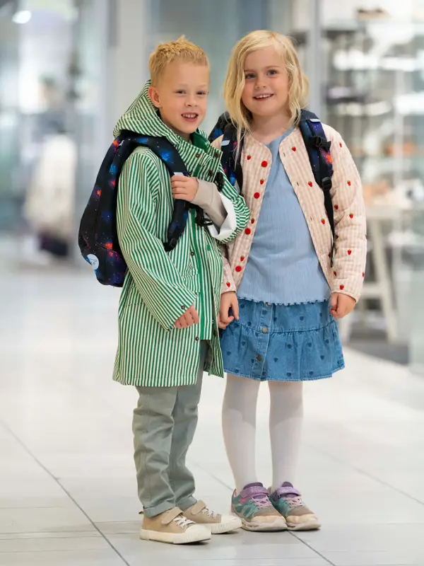 Gutt og jente står ved siden av hverandre på et kjøpesenter med yttertøy og skolesekker