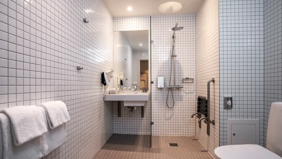 Handicapvennlig baderom med håndklær, toalett, servant, dusj og dusjstol