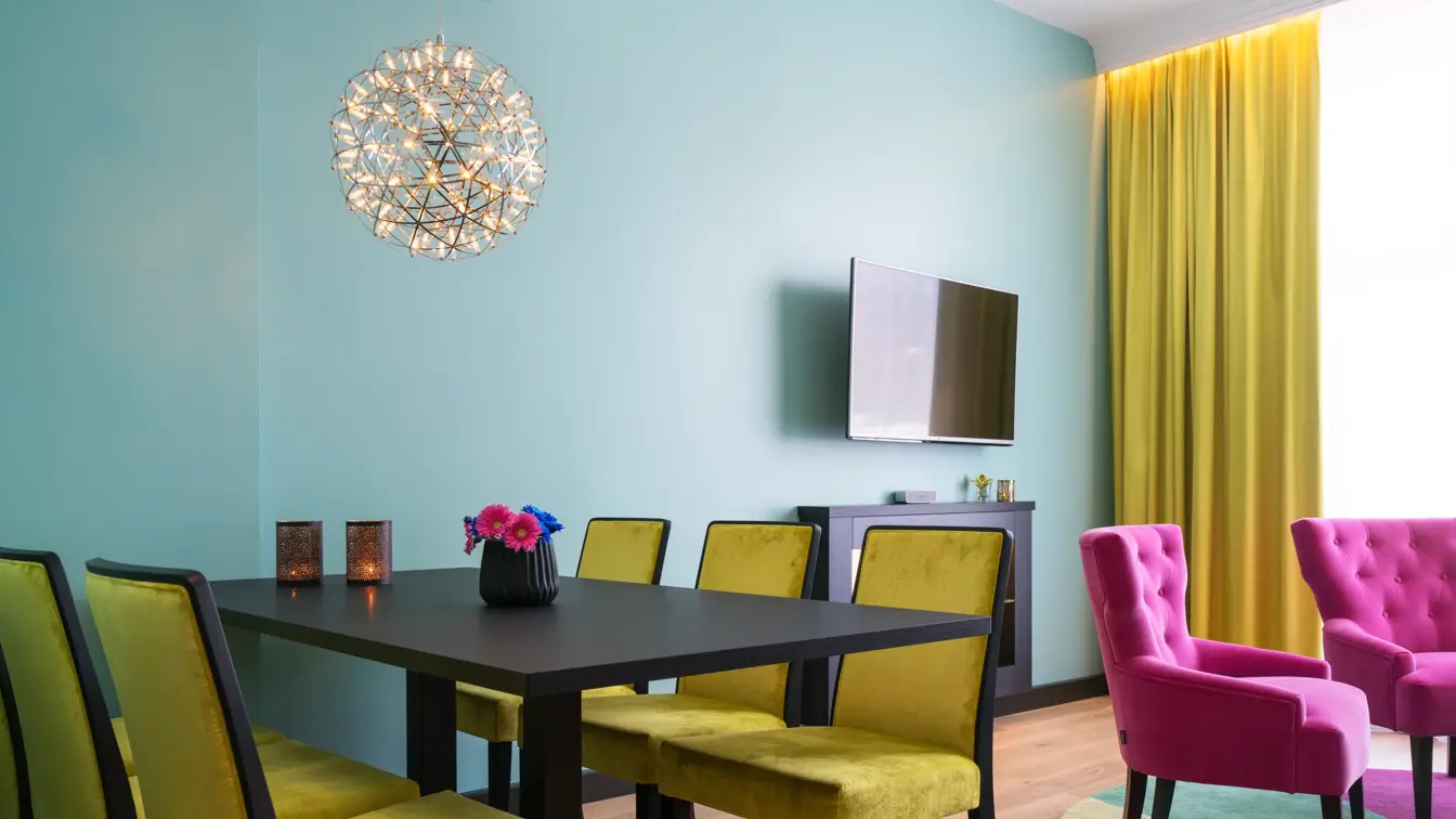 Langbord med lyskrone og seks sitteplasser, tv og sittegruppe i bakgrunnen på suite på Thon Hotel Terminus i Oslo sentrum nær Jernbanetorget