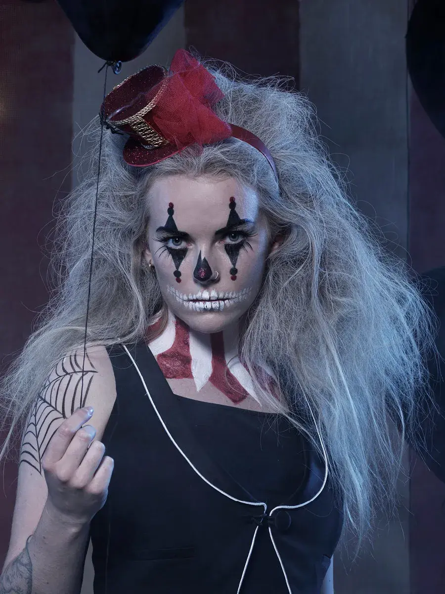 dame med bustete hår, ansiktsmaling, rød hatt og svart overdel holder en svart ballong