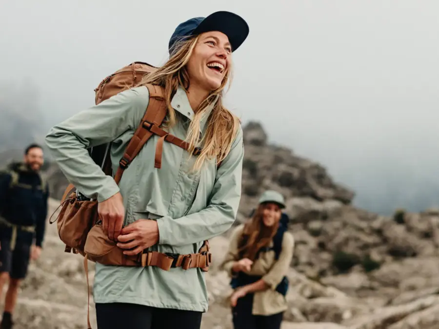 Dame som smiler med friluftsklær med to andre på et fjell