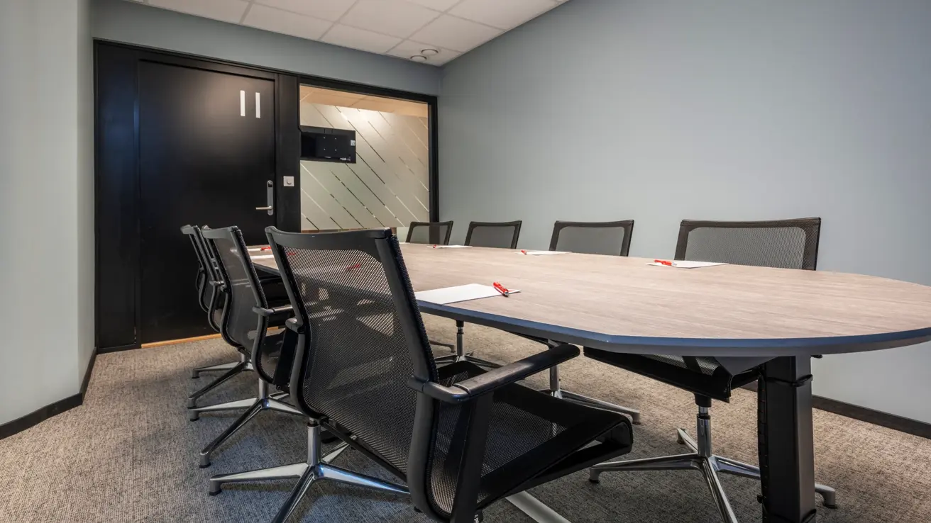 Møterom med styrebords oppsett til 8 personer. Grått bord og svarte kontorstoler rundt.
