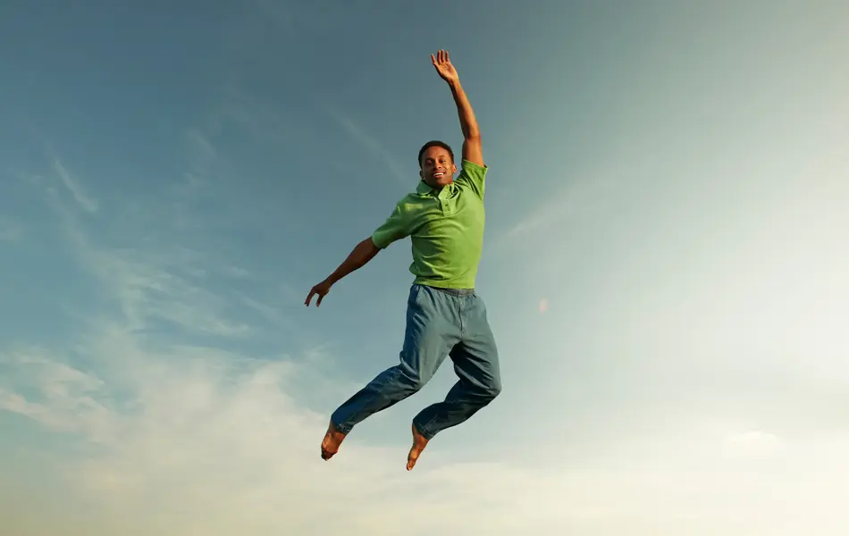 Mann med slimgrønn skjorte hopper i luften og smiler til kamera 