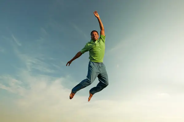 Mann med slimgrønn skjorte hopper i luften og smiler til kamera 