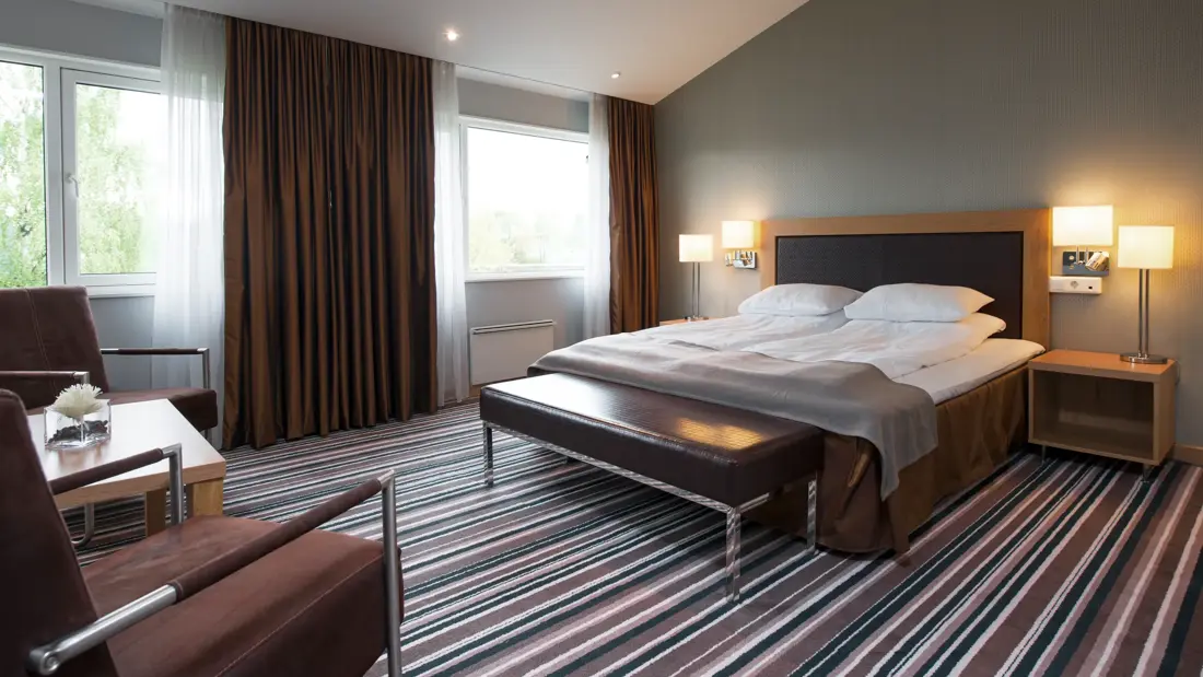 Dobbeltseng, to lenestoler, stripete teppe på gulvet og mye gulvplass på Thon Hotel Vettre i Asker