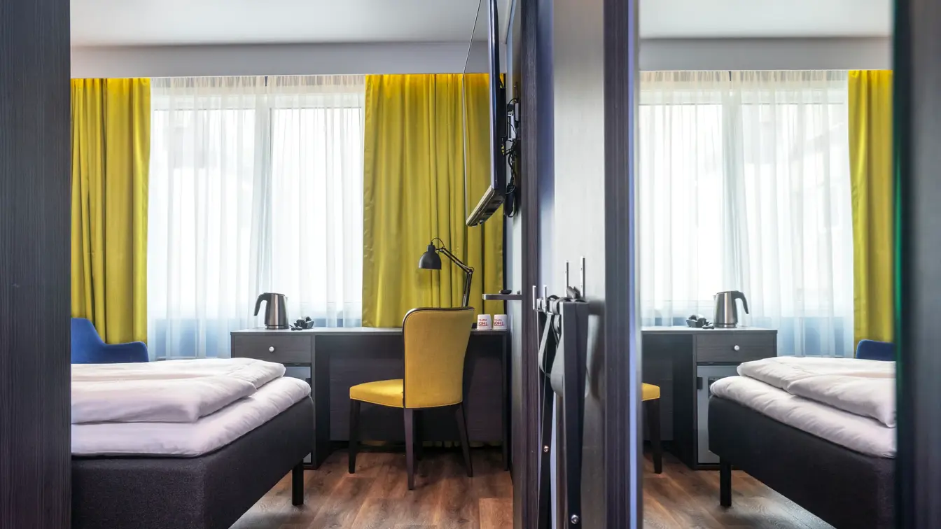 Gule gardiner, parkettgulv, gul stol, blomstertapet vegg, vindu, skrivebordpult, TV, dobbeltseng, speil