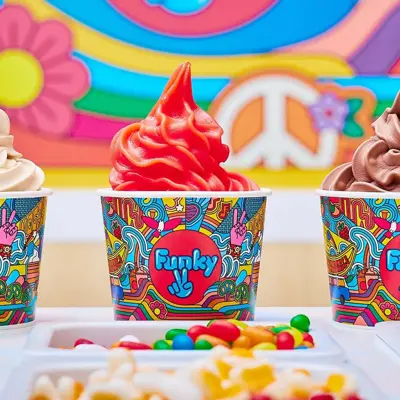 tre ulike frozen yoghurt i papp kopp stående på en disk med flere ulike topping