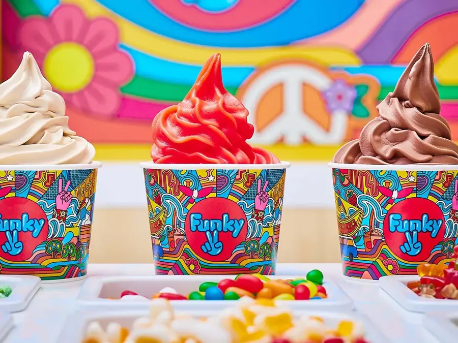 tre ulike frozen yoghurt i papp kopp stående på en disk med flere ulike topping