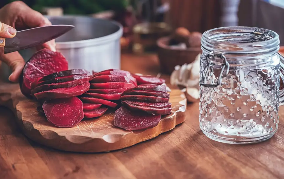 Mann skjærer kokte rødbeter i skiver på et skjærebrett