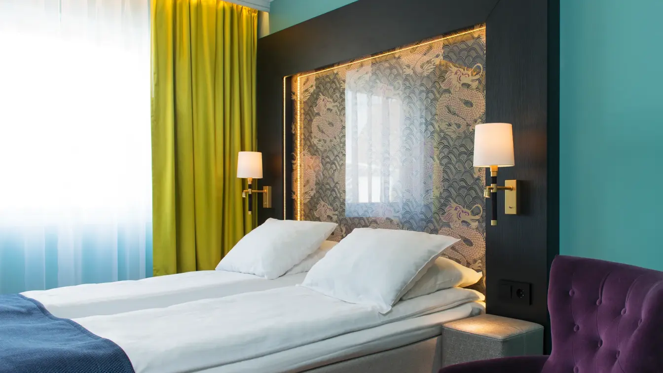 Dobbeltseng med en lilla stol og gule gardiner på Thon hotel Terminus i Oslo sentrum nær Jernbanetorget