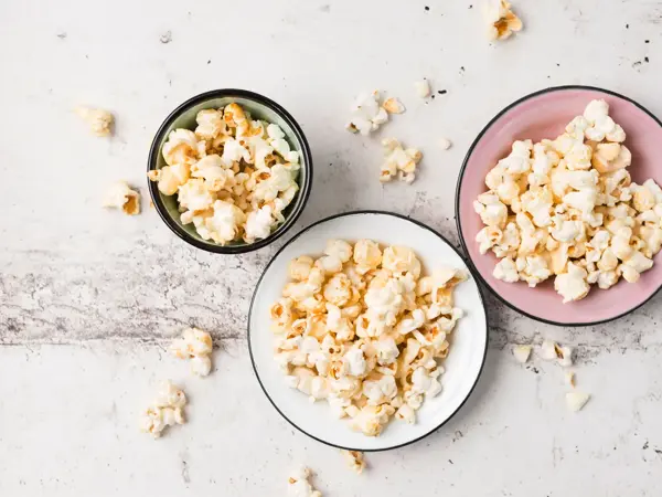 En hvit, en grønn og en rosa skål, alle fylt med popkorn
