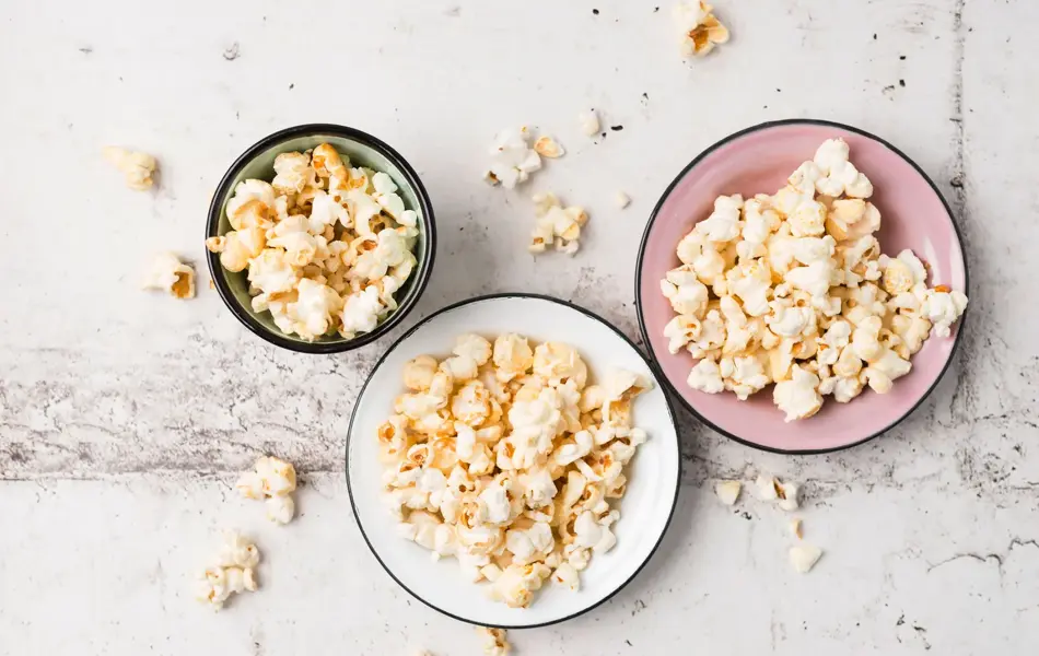 En hvit, en grønn og en rosa skål, alle fylt med popkorn