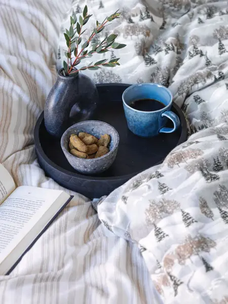 Kaffe og godteri på et matfat i en seng og en åpen bok