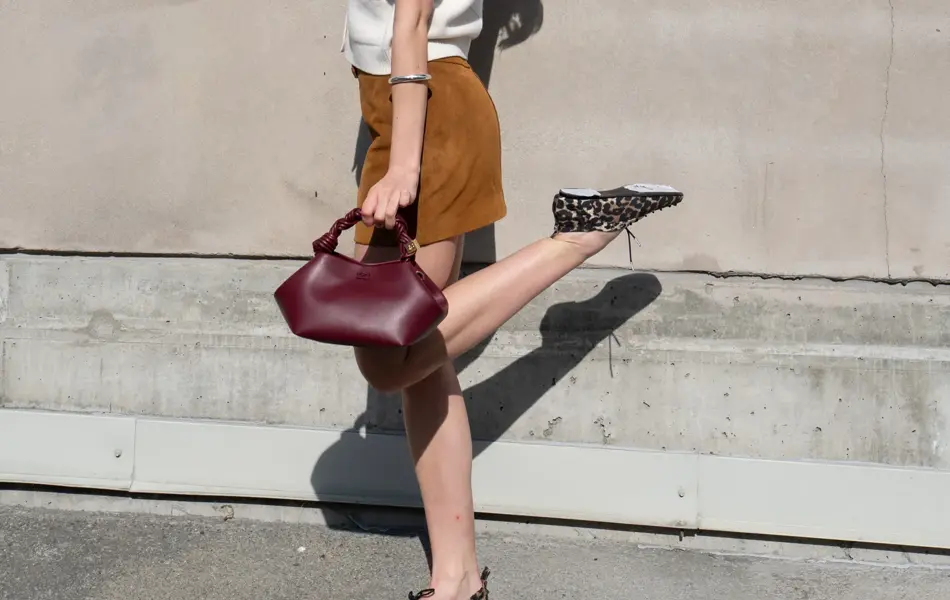 Ung dame i hvit kortermet strikketopp, brun semsket kort skjørt, burgunder veske og flate sko i leopardmønster