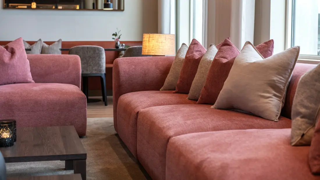 Lyserød sofagruppe med puter i lobbyområde.