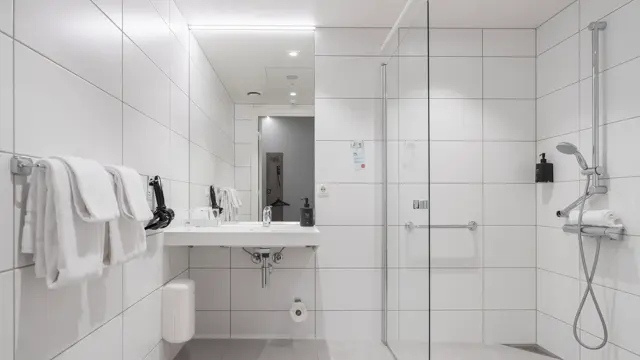 Flislagt bad med dusj, servant med speil over, og håndklær på veggen