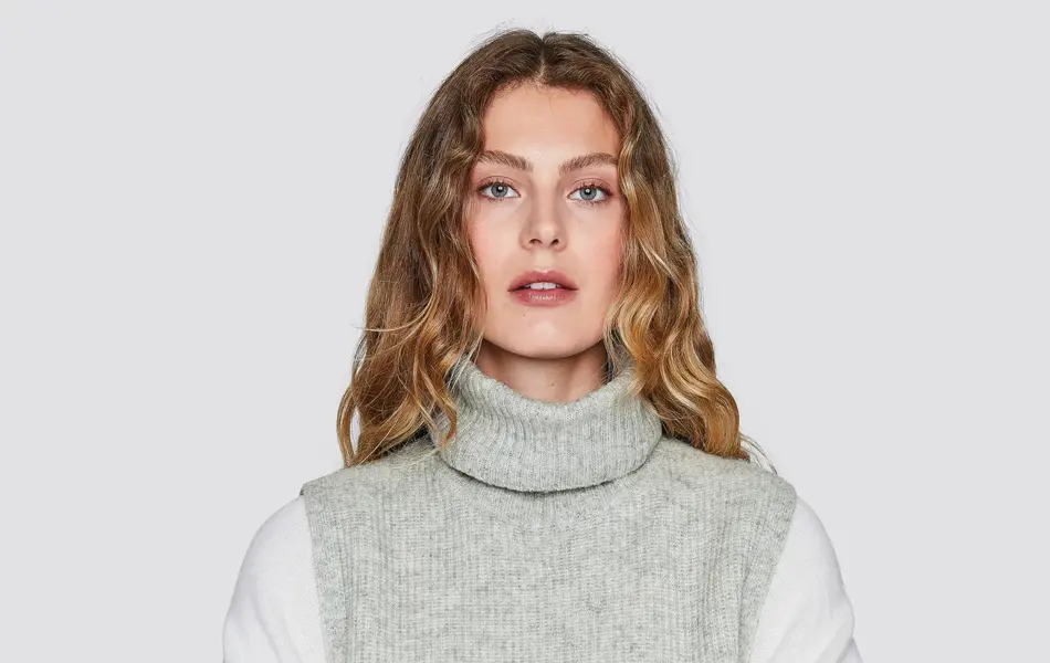 Kvinnelig modell som poserer i hvit genser med en strikket, grå hals o ver