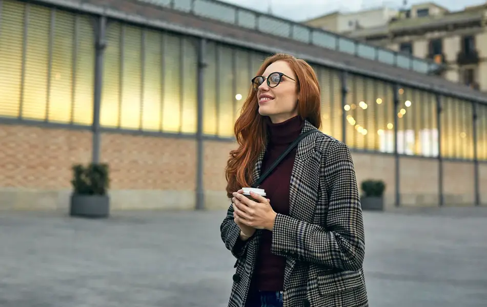 Dame i grå, hvit og svart jakke holder en kaffekopp
