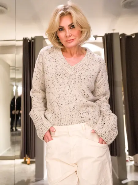 Dame i beige melert strikkegenser og hvite bukser