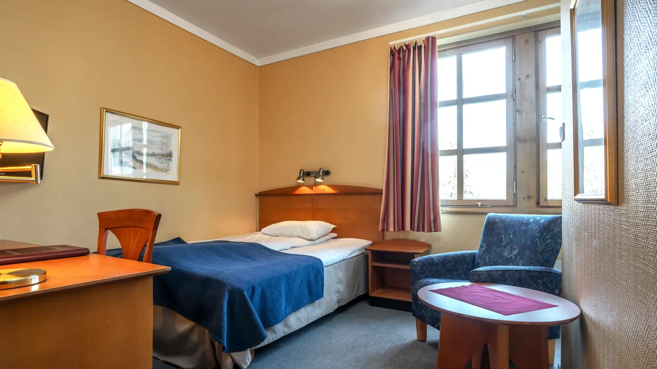 Enkeltseng med skrivebord og stol med et lite bord på siden