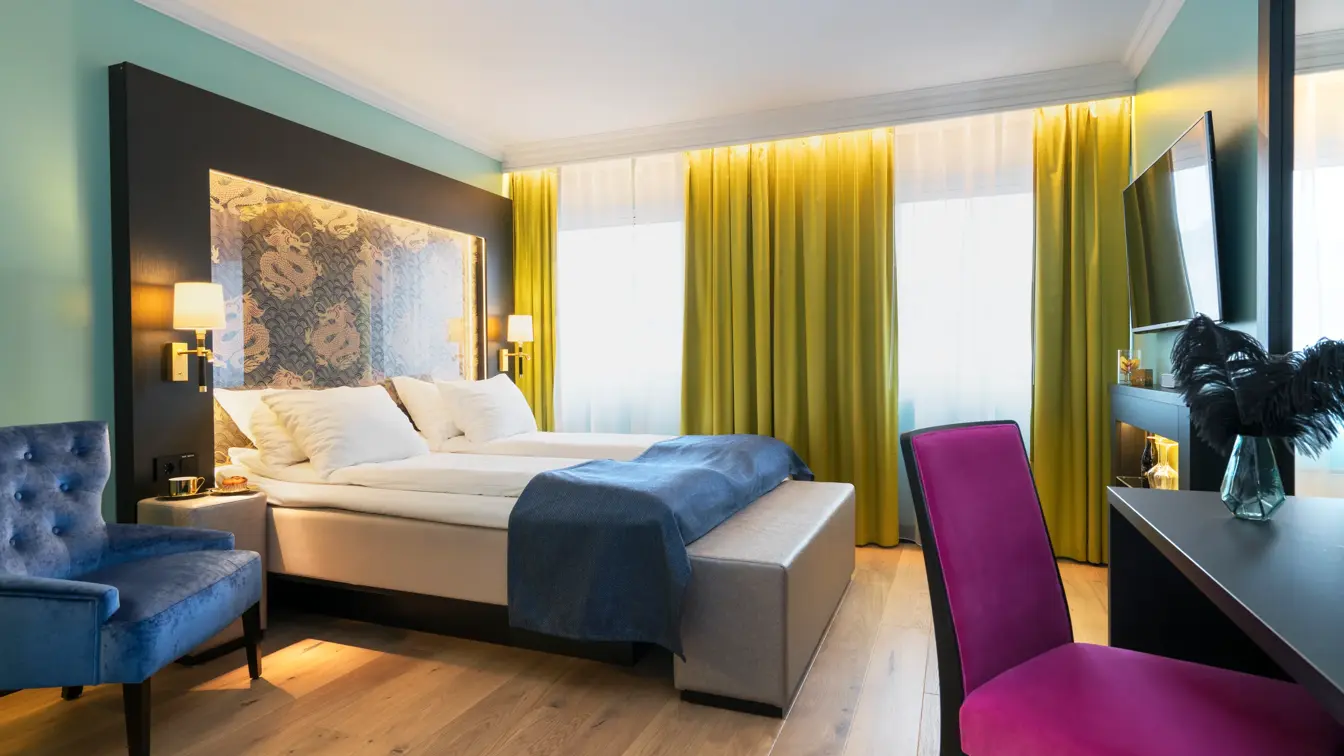Dobbeltseng, blå lenestol, skrivepult med lilla stol og TV på Thon hotel Terminus i Oslo sentrum nær Jernbanetorget