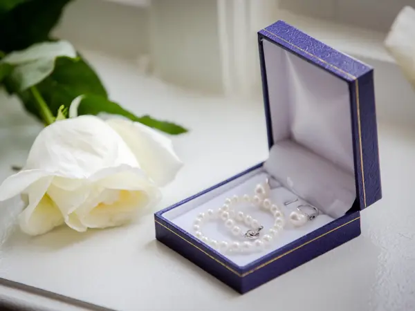 Blå boks med perlesmykker ved siden av en hvit rose
