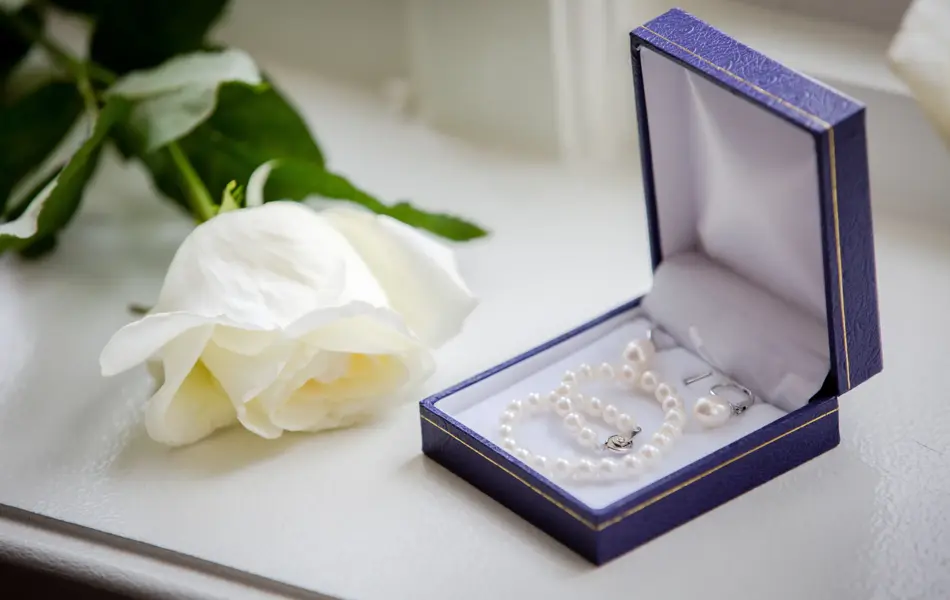 Blå boks med perlesmykker ved siden av en hvit rose