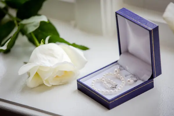 Blå boks med perlesmykker ved siden av en hvit rose