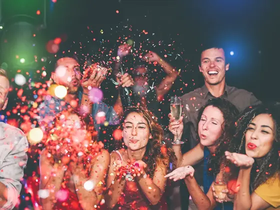 Folkemengde blåser fargerikt konfetti mot kamera. Foto til artikkel om å arrangere nyttårsfest