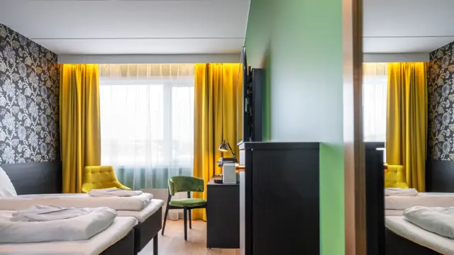 Separate senger, mørk mønstrete tapet med blomster, gule gardiner, gul stol, skrivebord med kaffemaskin og grønn stol i superior twin rom på Thon Hotel Kirkenes
