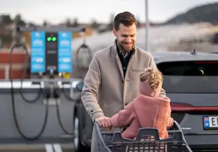 Far triller på en handlevogn med barnet sittende oppi på en parkeringsplass.
