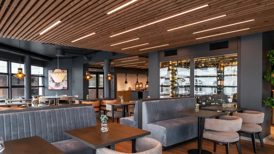 Frokostsal med firkantede bord, grå stoler og grå sittebenker.