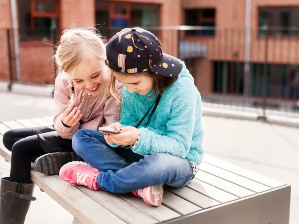 To jenter som sitter i skolegården mens de ser på en mobil