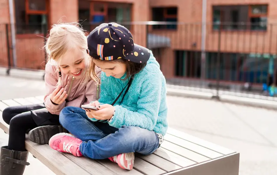 To jenter som sitter i skolegården mens de ser på en mobil